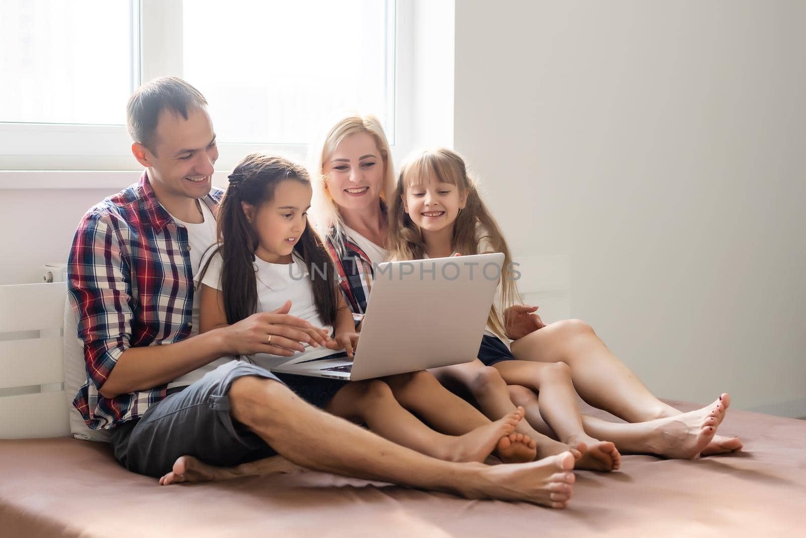 Happy family concept. Beautiful mother and handsome father with their daughters spending time together at home and lying on bed with laptop. by Andelov13