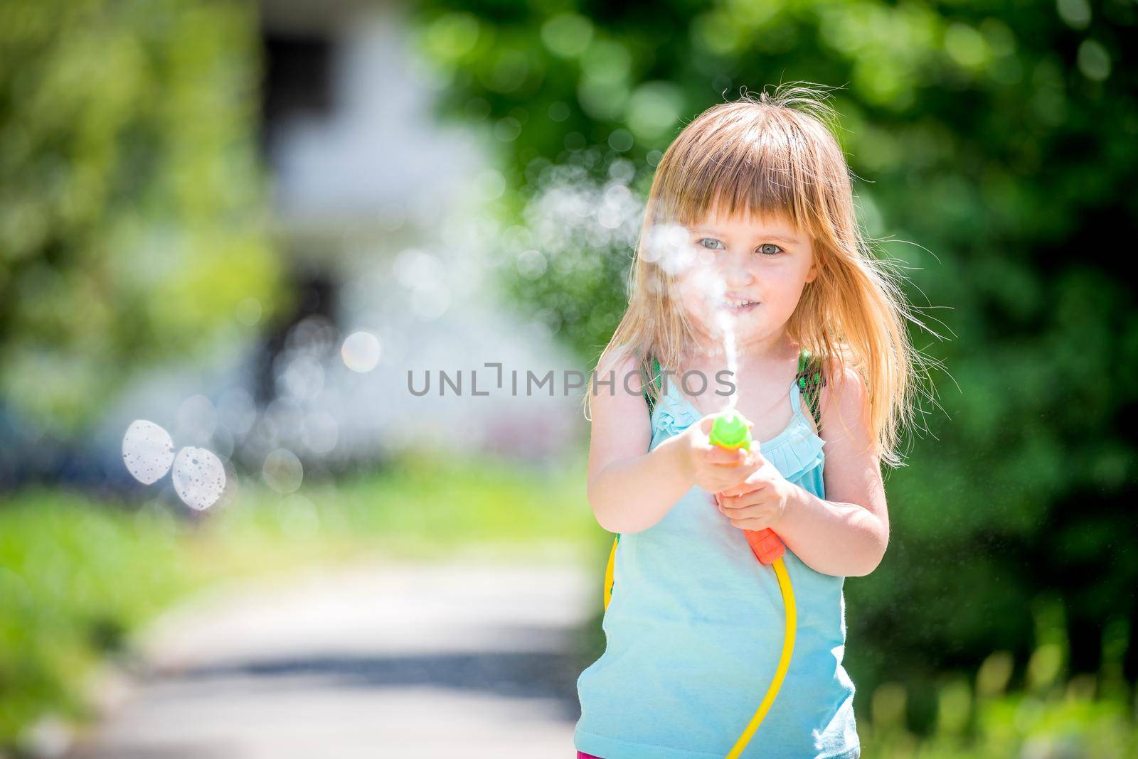 joyful little girl shooting with water pistol outside