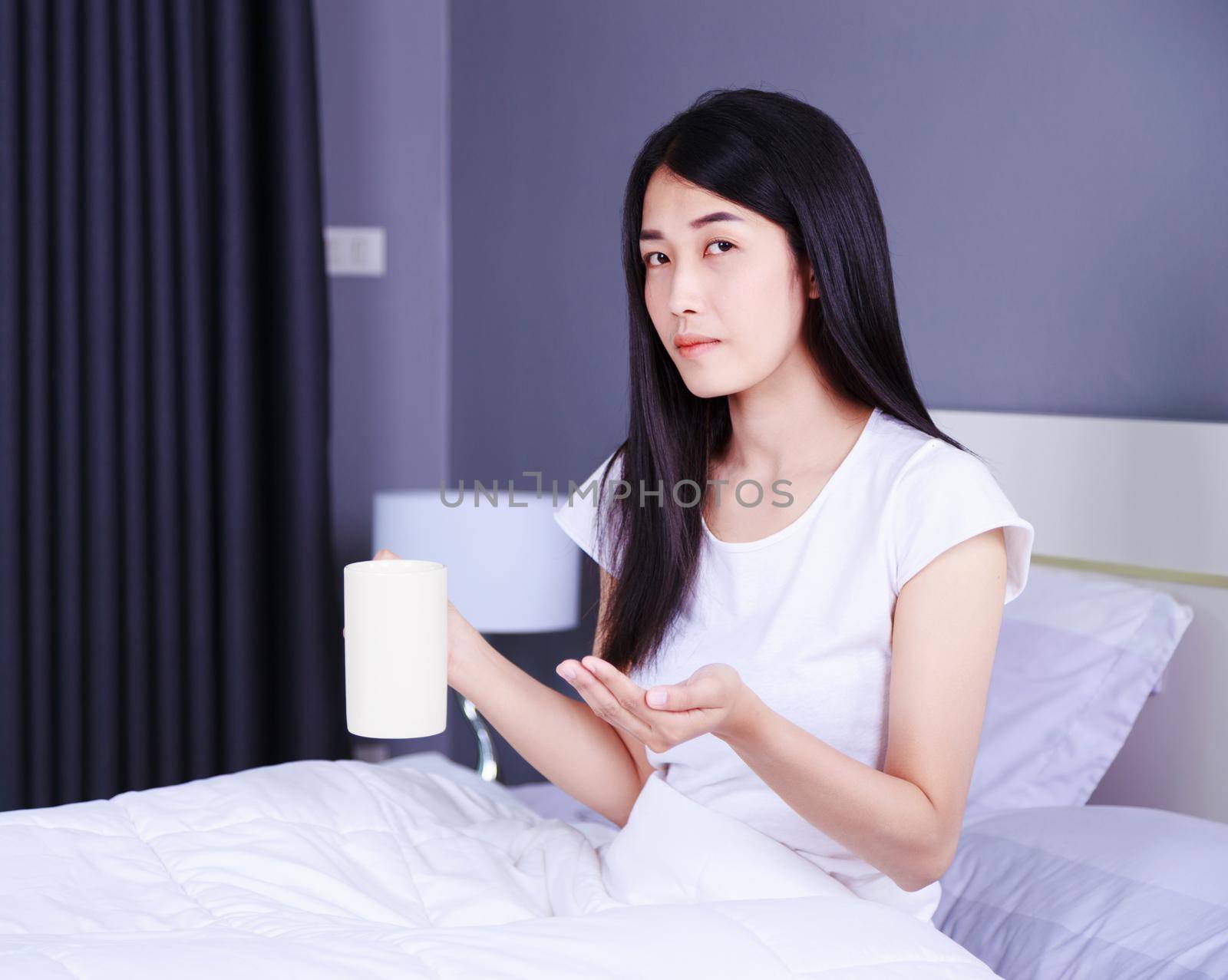 Woman taking pills and drink of water on bed in the bedroom