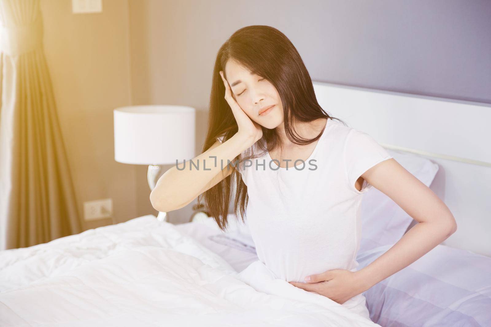 Woman stomach pain and headache on her bed in the bedroom