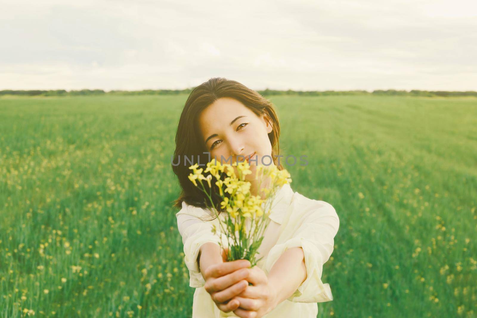 Beautiful young woman with a bouquet of yellow flowers on summer meadow. Focus on face
