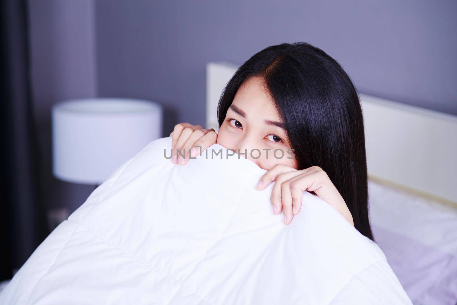 Woman hiding under a blanket on bed in the bedroom