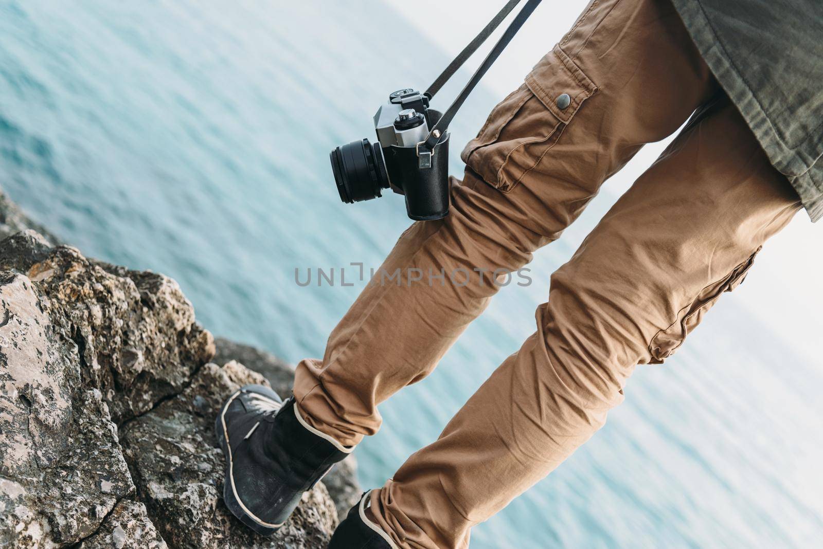 Traveler woman with old photo camera standing on stone coast near the sea. View of legs