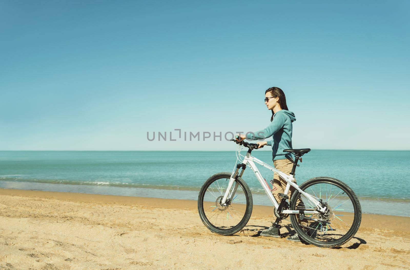 Beautiful young woman walking with a bicycle on beach in summer