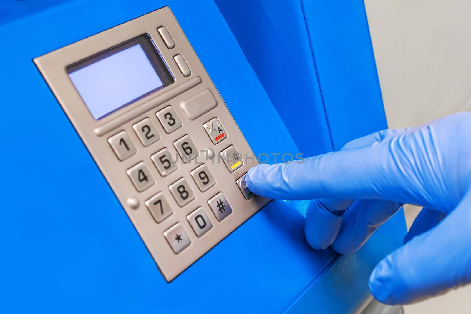 A man's hand in protective medical gloves dials a pincode at the terminal for issuing money, close-up.