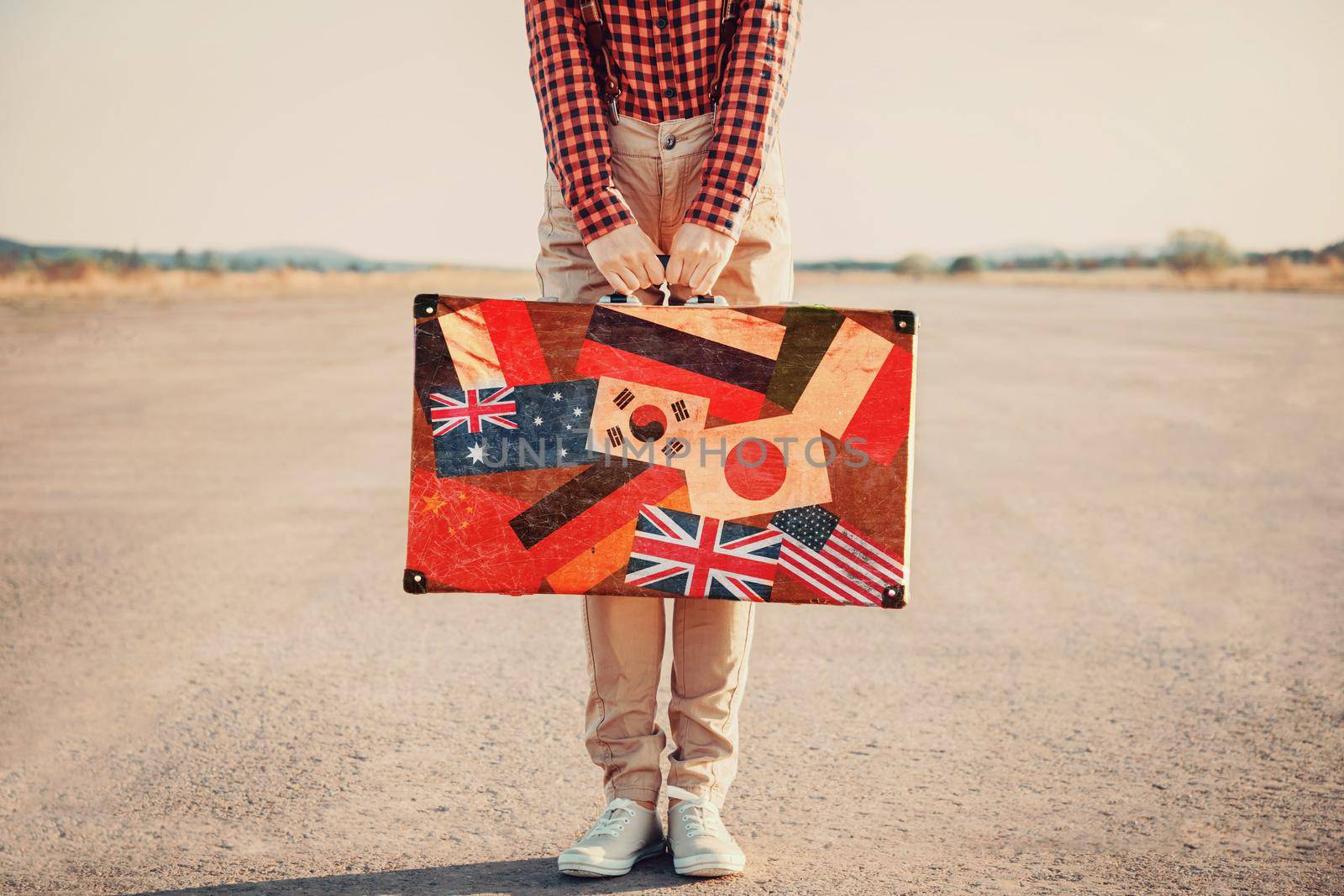 Traveler woman with a suitcase standing on road. Suitcase with stamps flags of different country