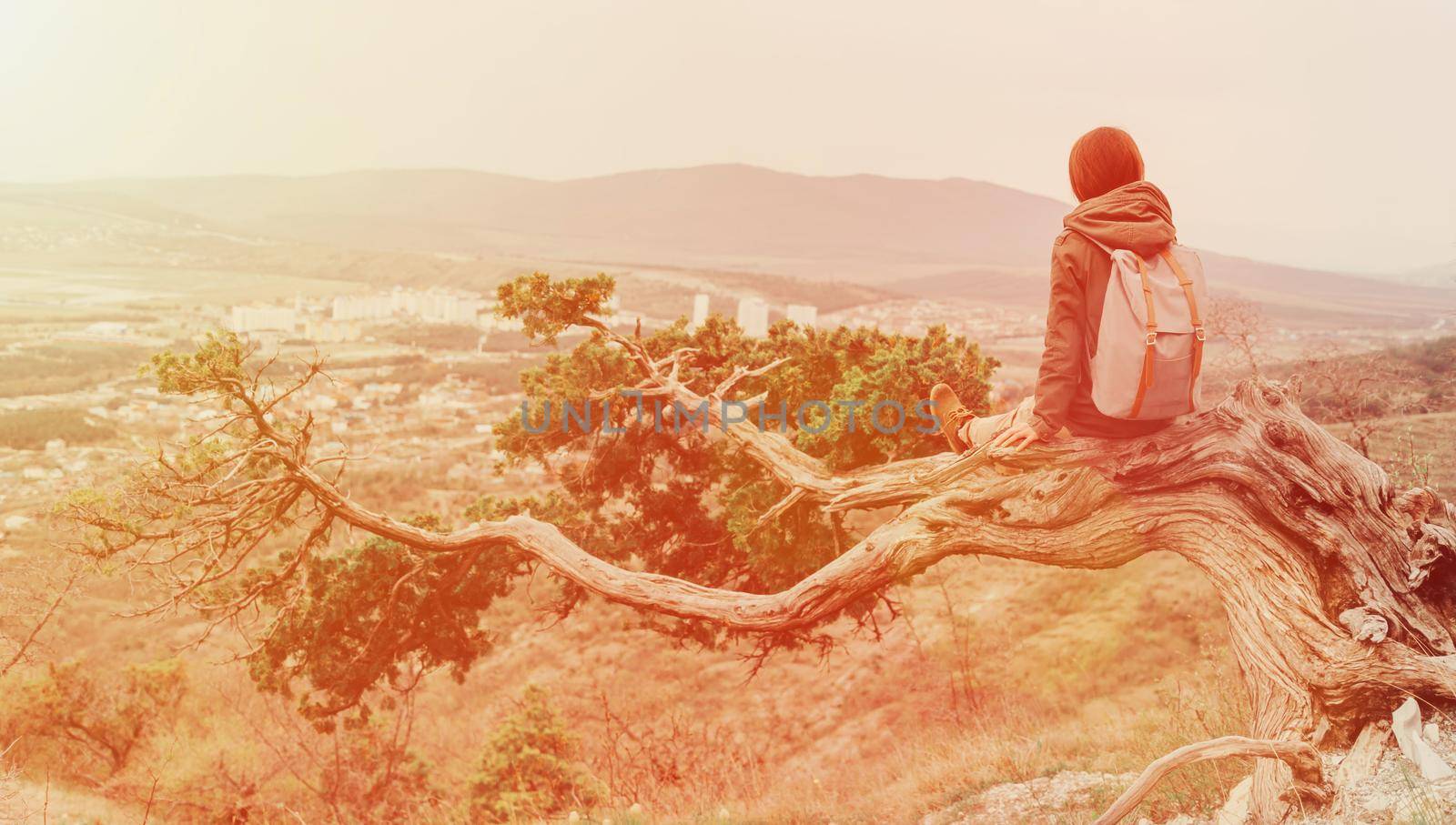 Traveler young woman sitting on a tree in the mountains. Image with sunlight effect