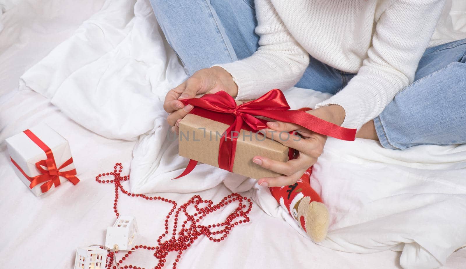 Woman wraps ecological Christmas gifts in wrapping paper, satin ribbon, sitting in a white bed with Christmas decorations. by Ekaterina34