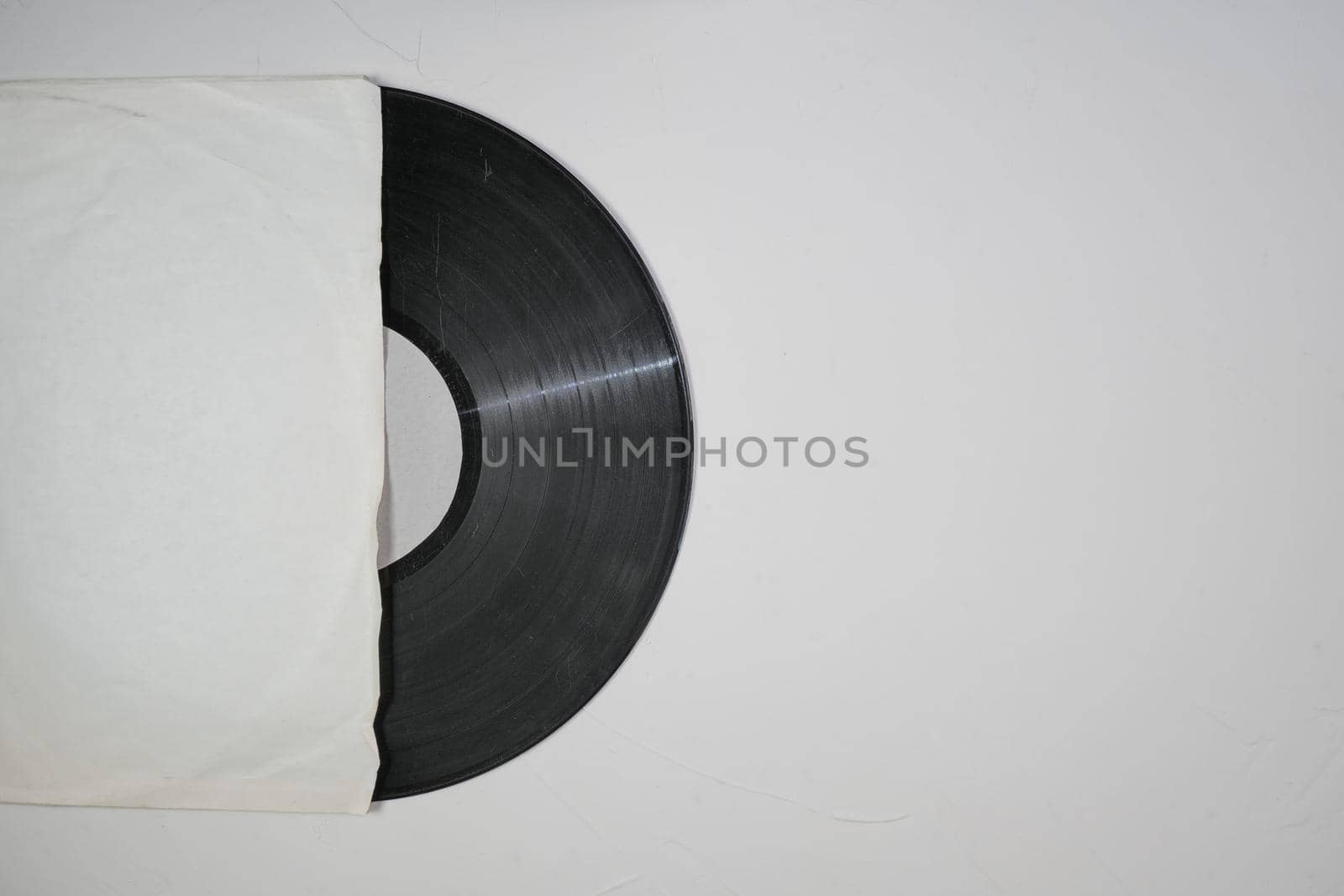 Old vinyl record in paper case on white marble background.