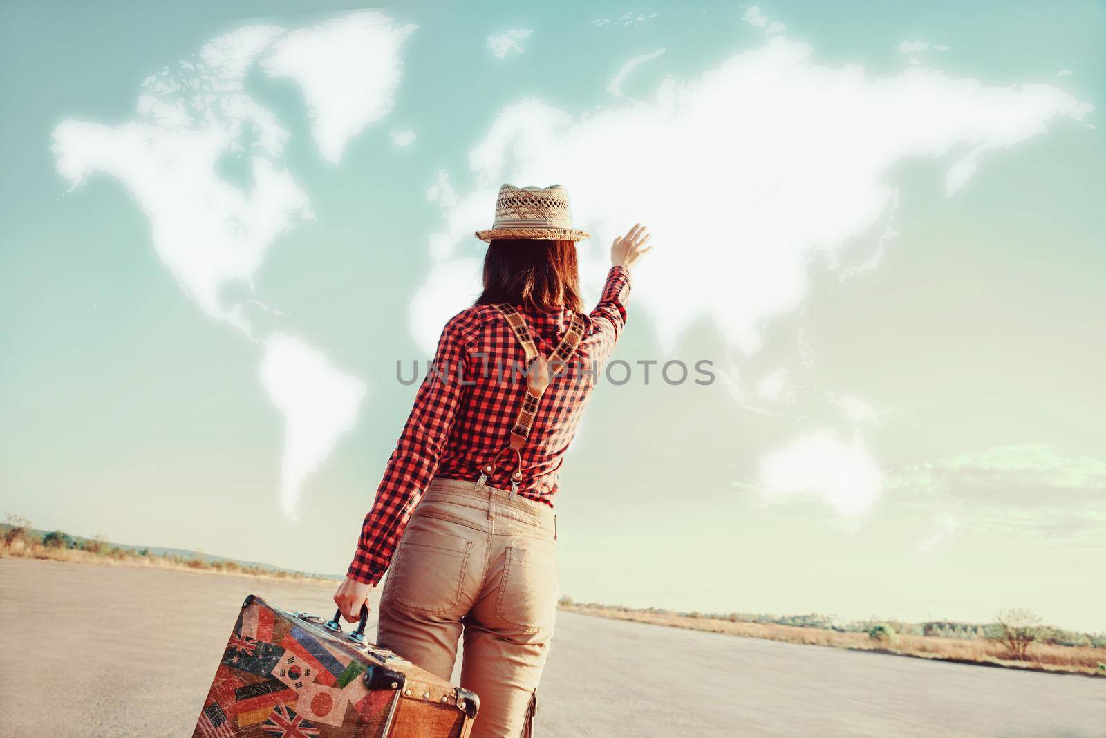 Traveler woman with vintage suitcase waves her hand to map of the world. Concept of travel