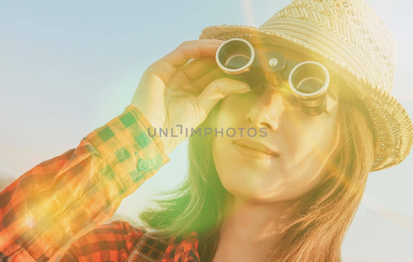 Smiling traveler young woman looking through binoculars outdoor. Image with sunlight effect