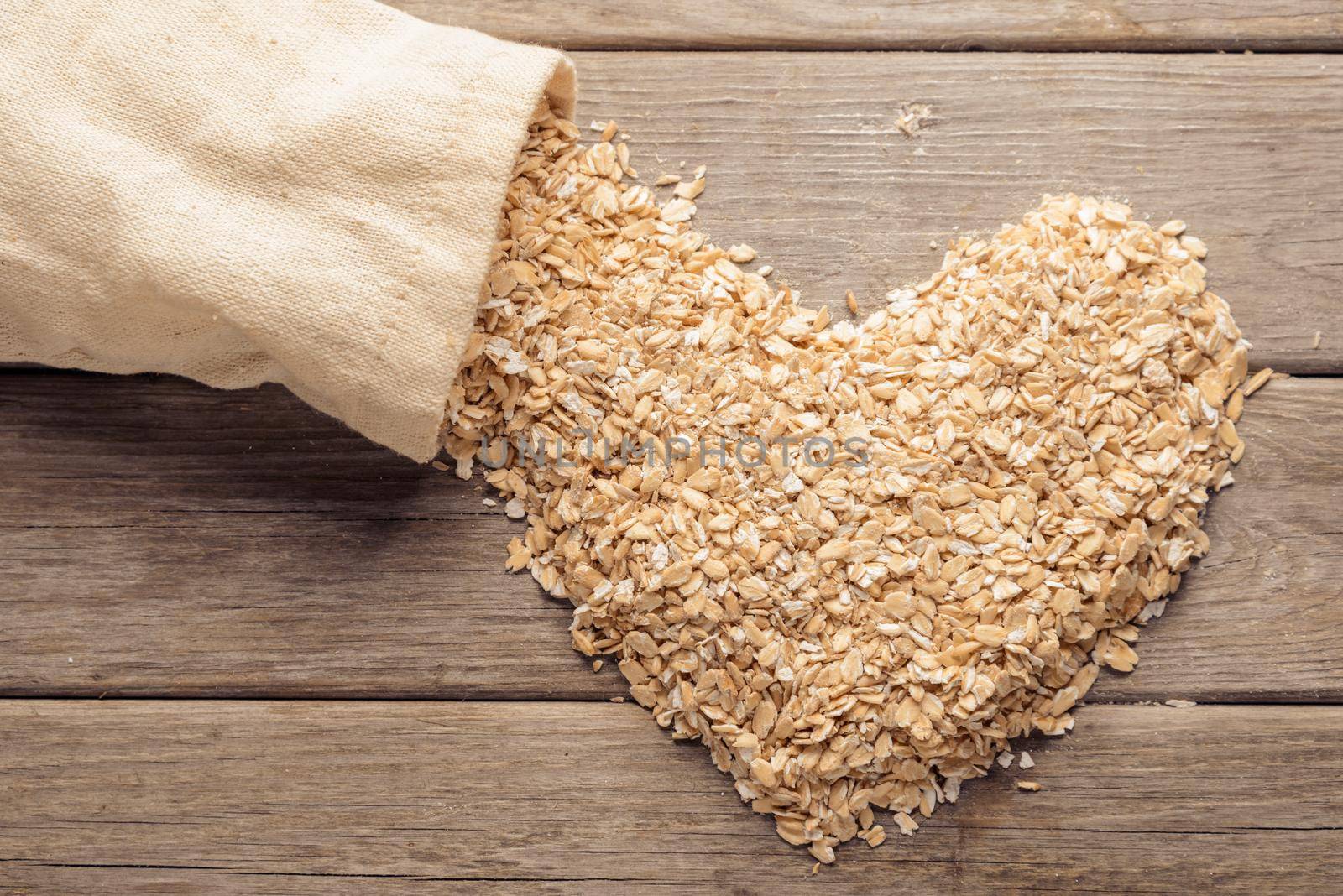 Heart shape of oatmeal flakes near a sack on a wooden table
