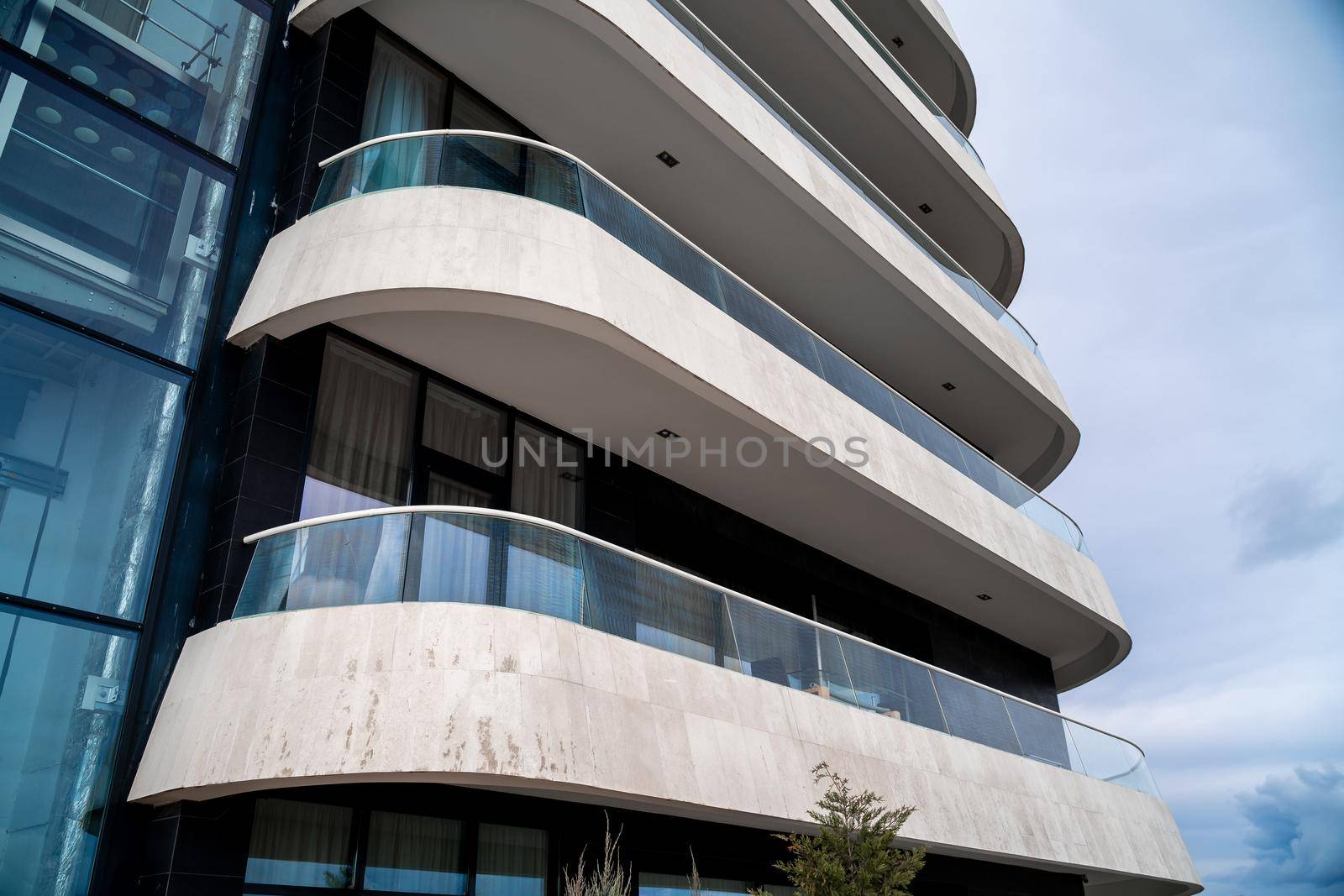 A corner of a modern building with a row of white balconies against the sky. On the left you can see the elevator. by Matiunina