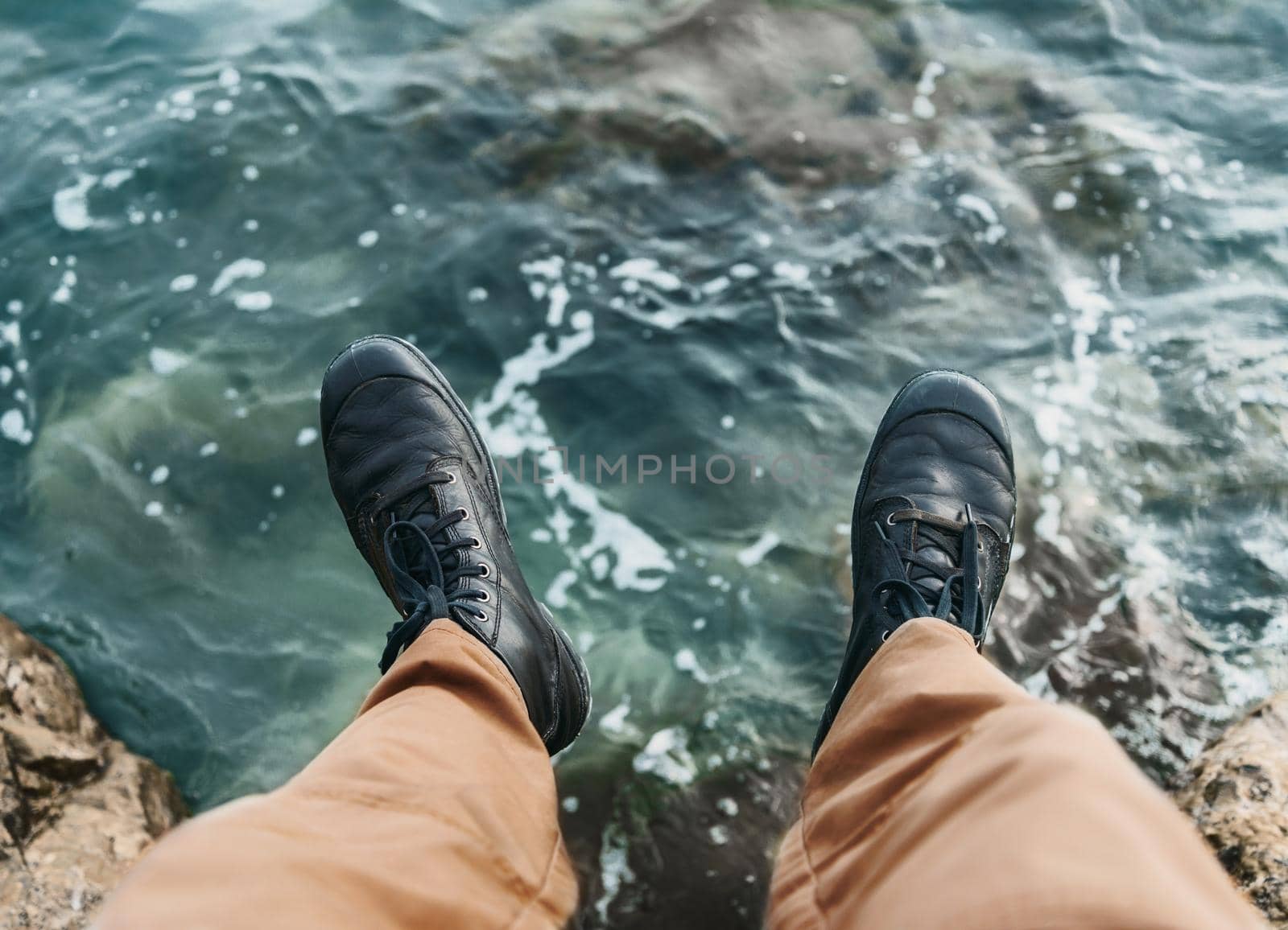 Man sitting on stone over the sea. View of legs. Point of view shot
