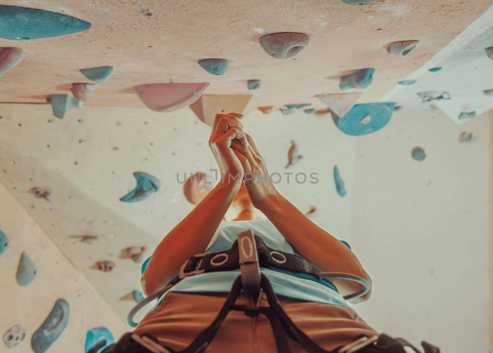 Climber woman coating her hands in powder chalk magnesium and preparing to climb indoor, view from below