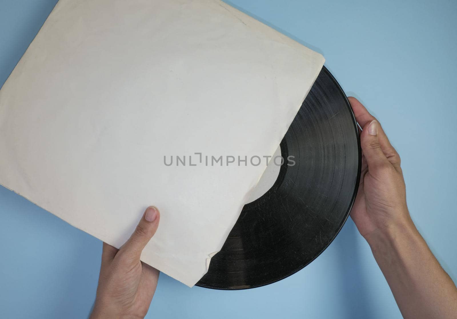 Hands hold an old vinyl record in an old paper case on a light blue background