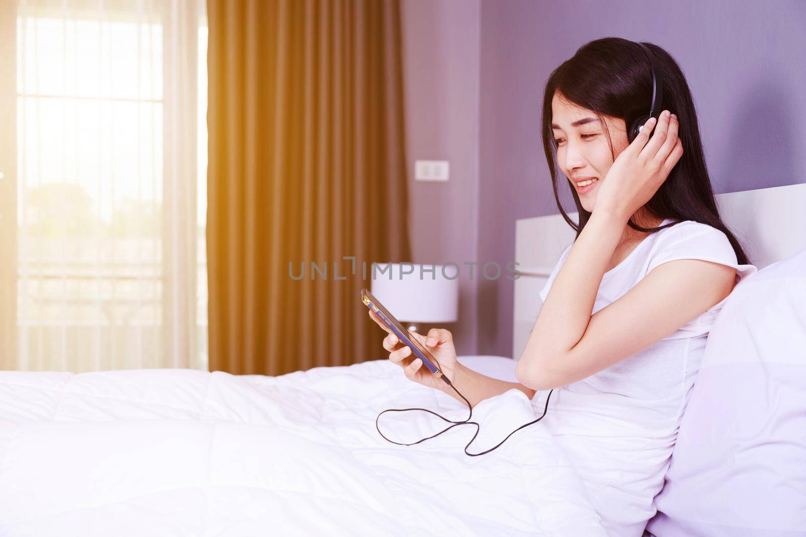 woman in headphones listening to music from smartphone on bed in the bedroom