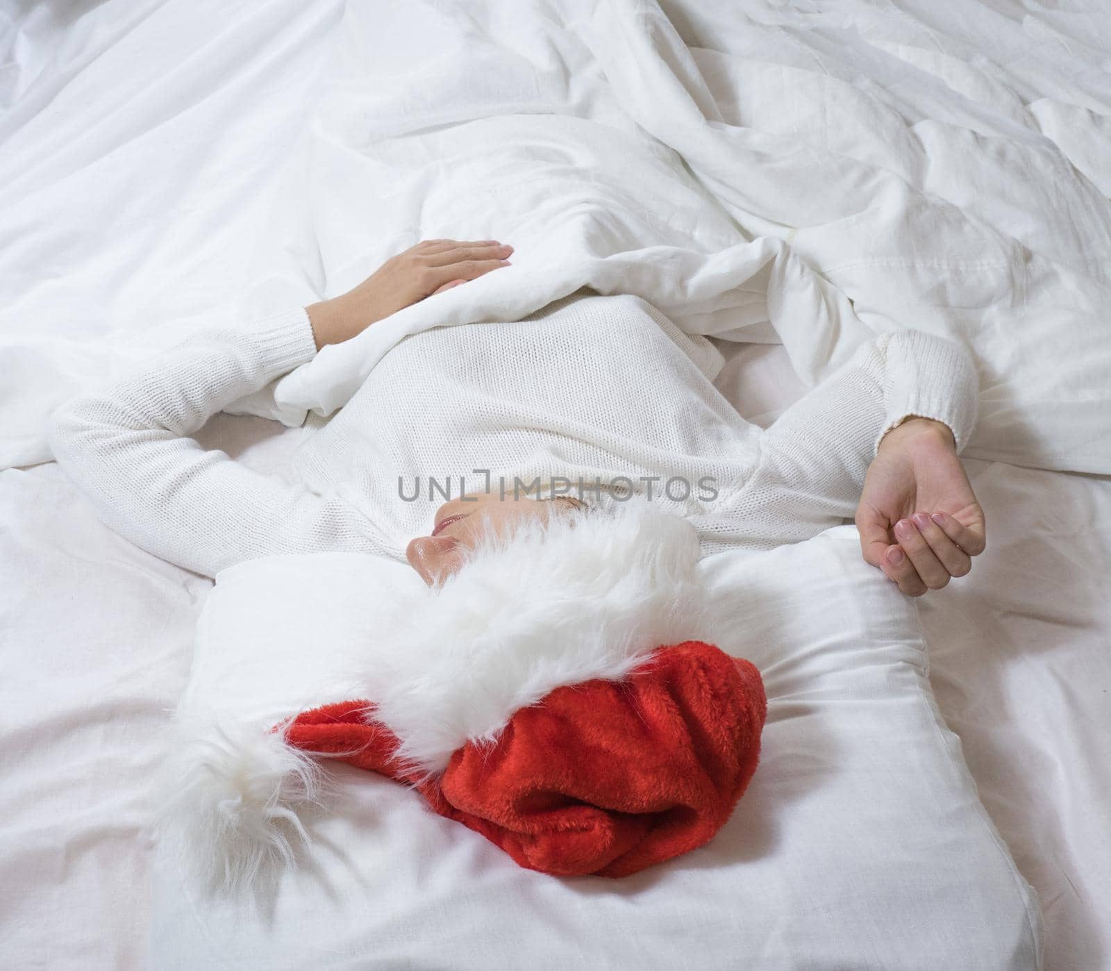 A brunette woman sleeps lying in a white bed in a Santa Claus hat. Merry Christmas