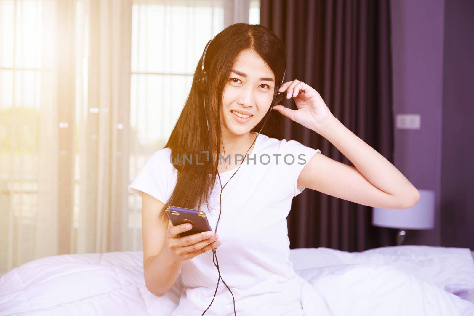 woman in headphones listening to music from smartphone on bed in the bedroom