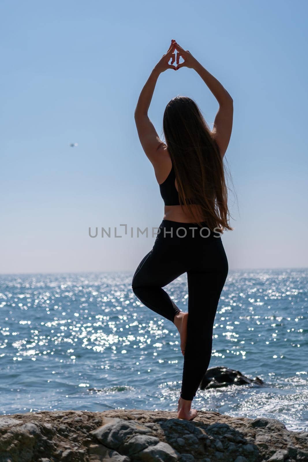 Woman makes heart with hands on beach. Young woman with long hair, fitness instructor, stretching before pilates, on a yoga mat near the sea on a sunny day, female fitness yoga routine concept by panophotograph