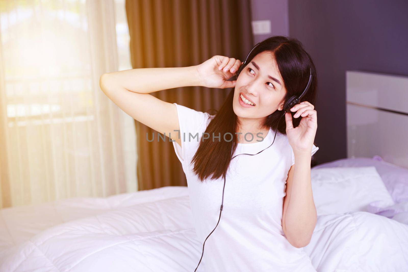 woman in headphones listening to music from smartphone on bed in the bedroom