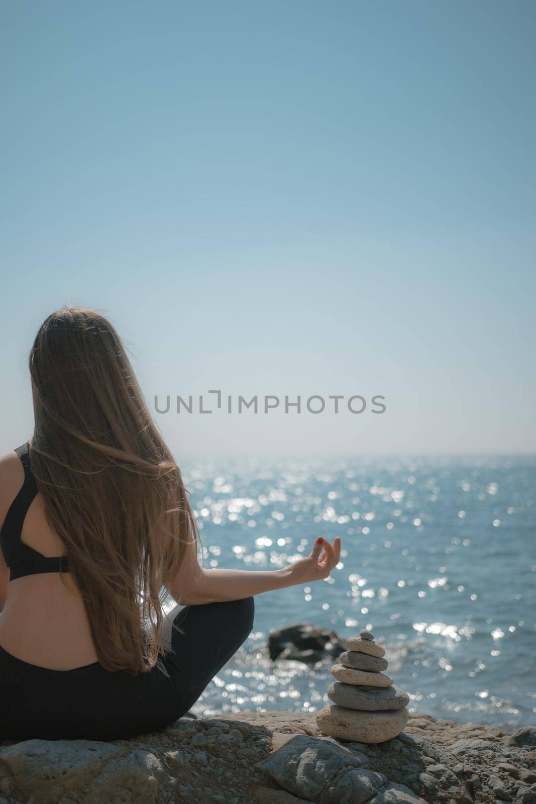 Young woman with long hair, fitness instructor in Sportswear Leggings and Tops, stretching before pilates, on a yoga mat near the sea on a sunny day, female fitness yoga routine concept by panophotograph