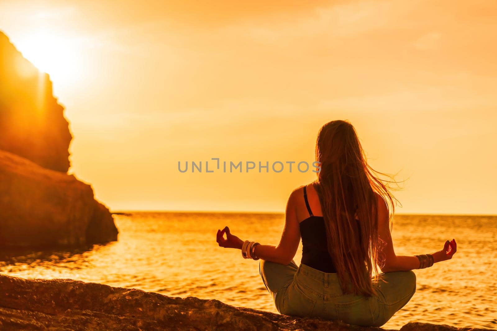 Young woman in swimsuit with long hair practicing stretching outdoors on yoga mat by the sea on a sunny day. Women's yoga fitness pilates routine. Healthy lifestyle, harmony and meditation concept.