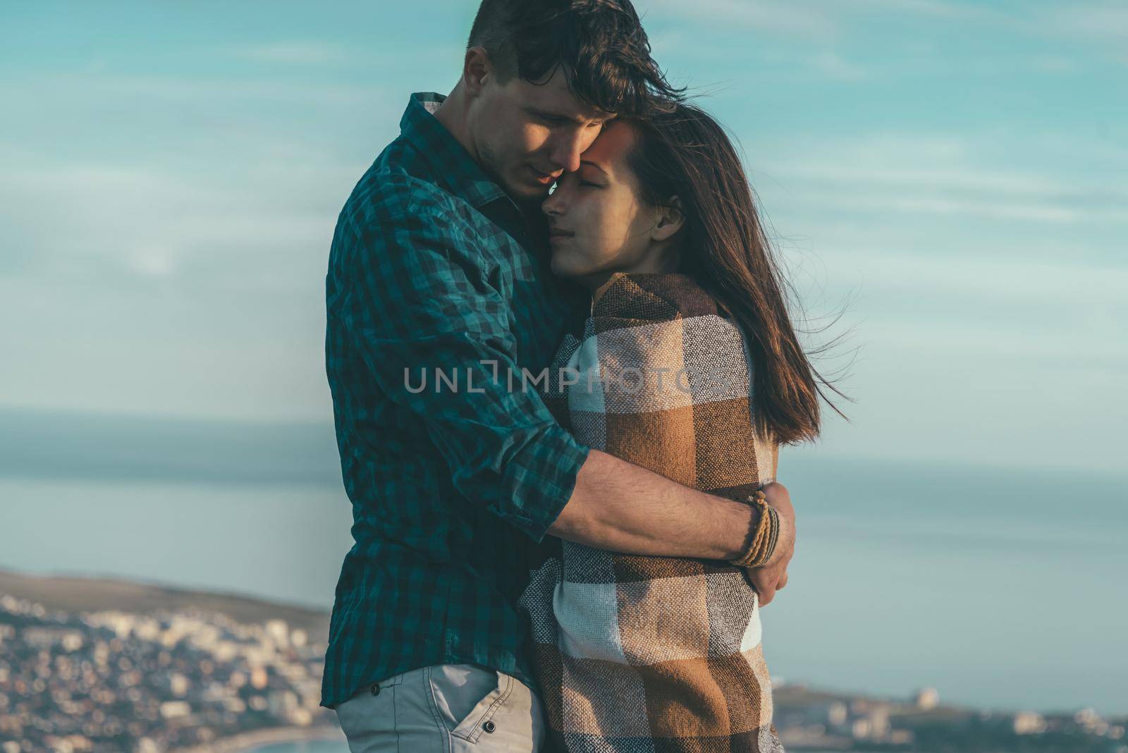 Couple in love. Young man embraces a woman wrapped in plaid on background of sea, tranquil scene