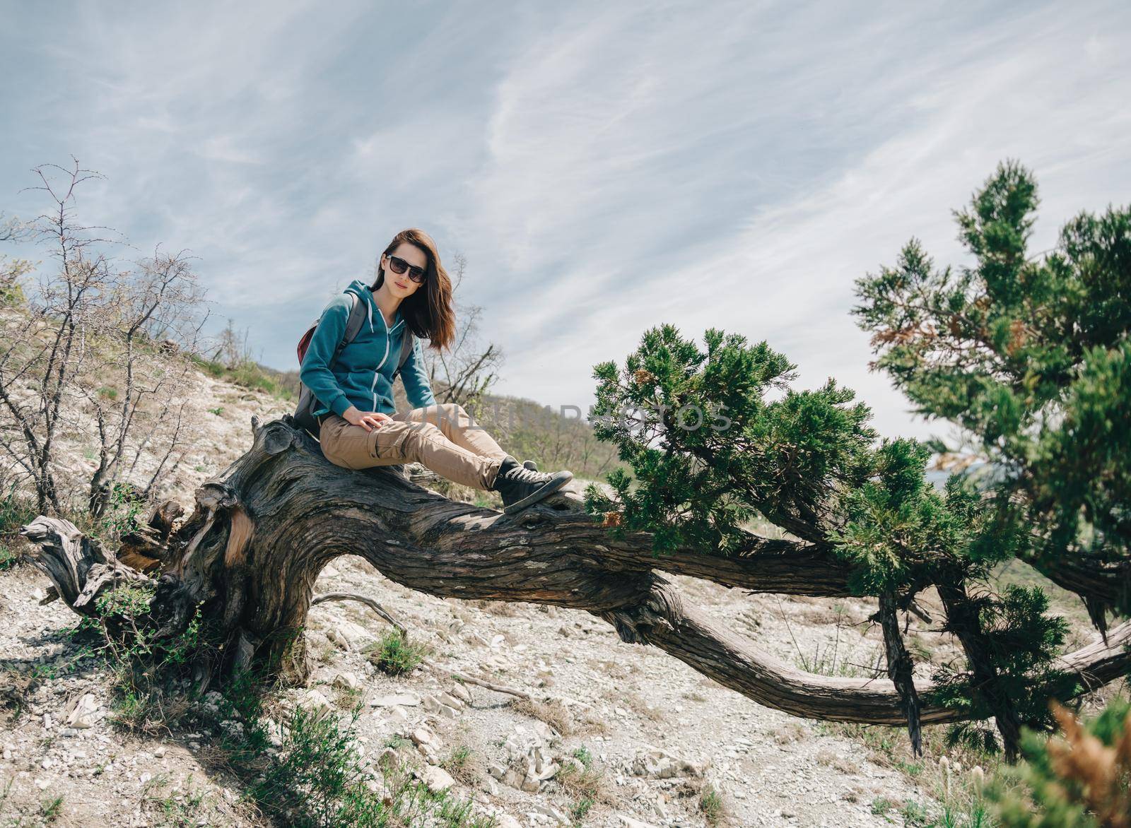 Beautiful young woman sitting on fairy old tree in summer