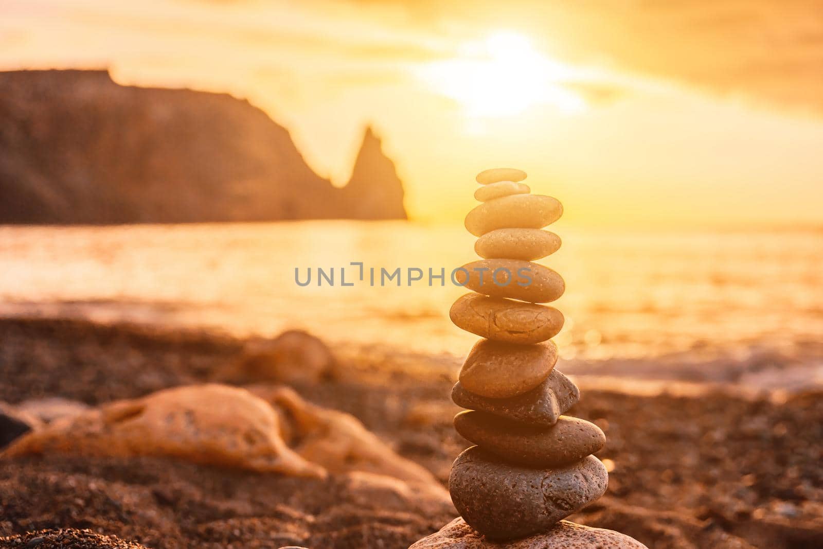 Balanced pebble pyramid on the beach on a sunset time. Sea waves and foam on the background. Selective focus. Zen stones on the sea beach, meditation, spa, harmony, calmness, balance concept by panophotograph