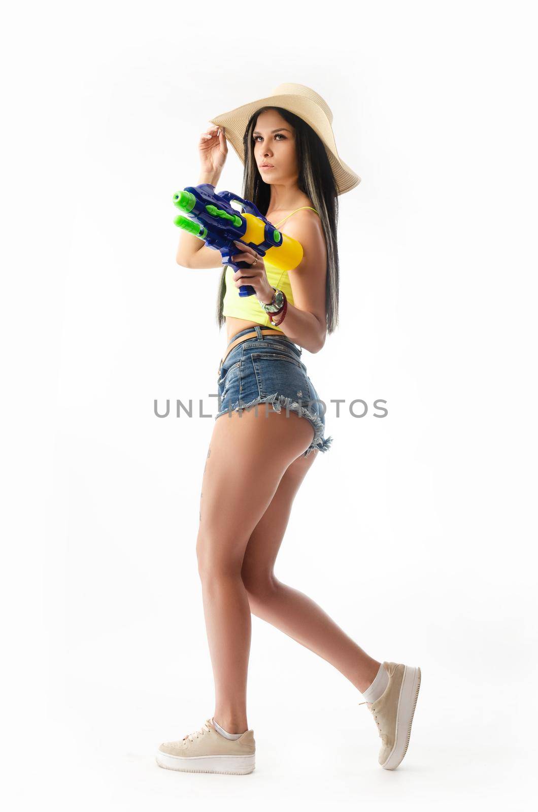 brunette girl with a water gun in summer clothes, slim and sexy isolated on a white background