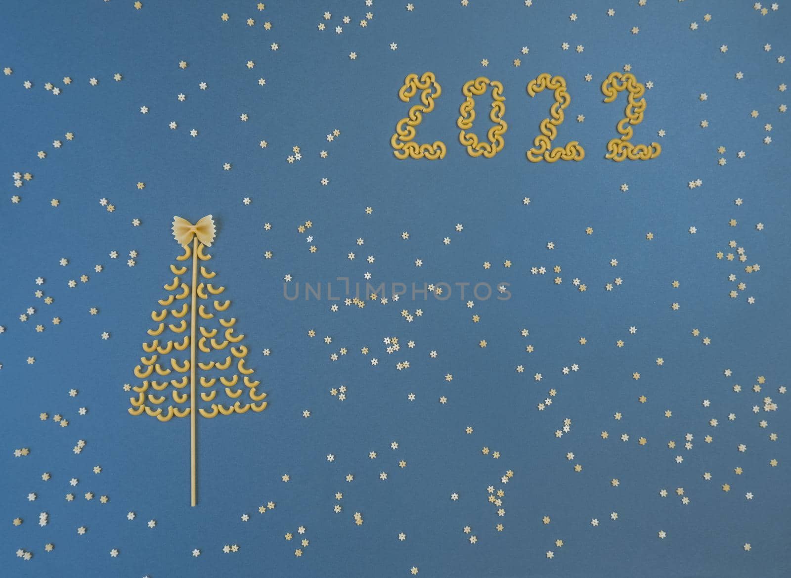 Christmas tree lined with dry pasta and numbers 2022 and stars from pasta on a blue paper background. by Ekaterina34