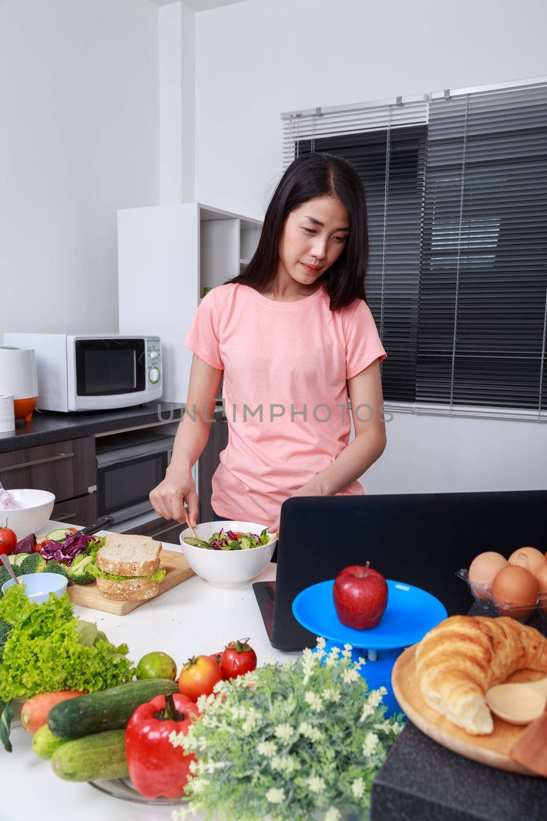 young woman mixing salad while cooking with laptop in kitchen 