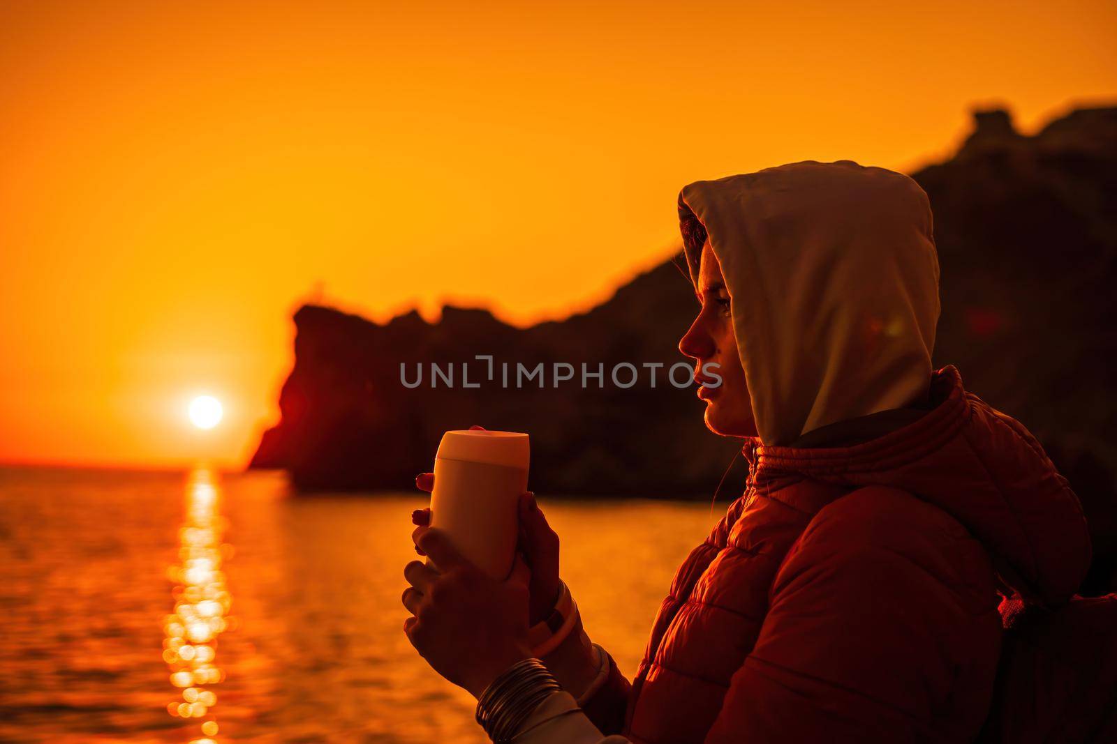 woman traveler drinks coffee with a view of the mountain landscape. A young tourist woman drinks a hot drink from a cup and enjoys the scenery in the mountains. Trekking concept