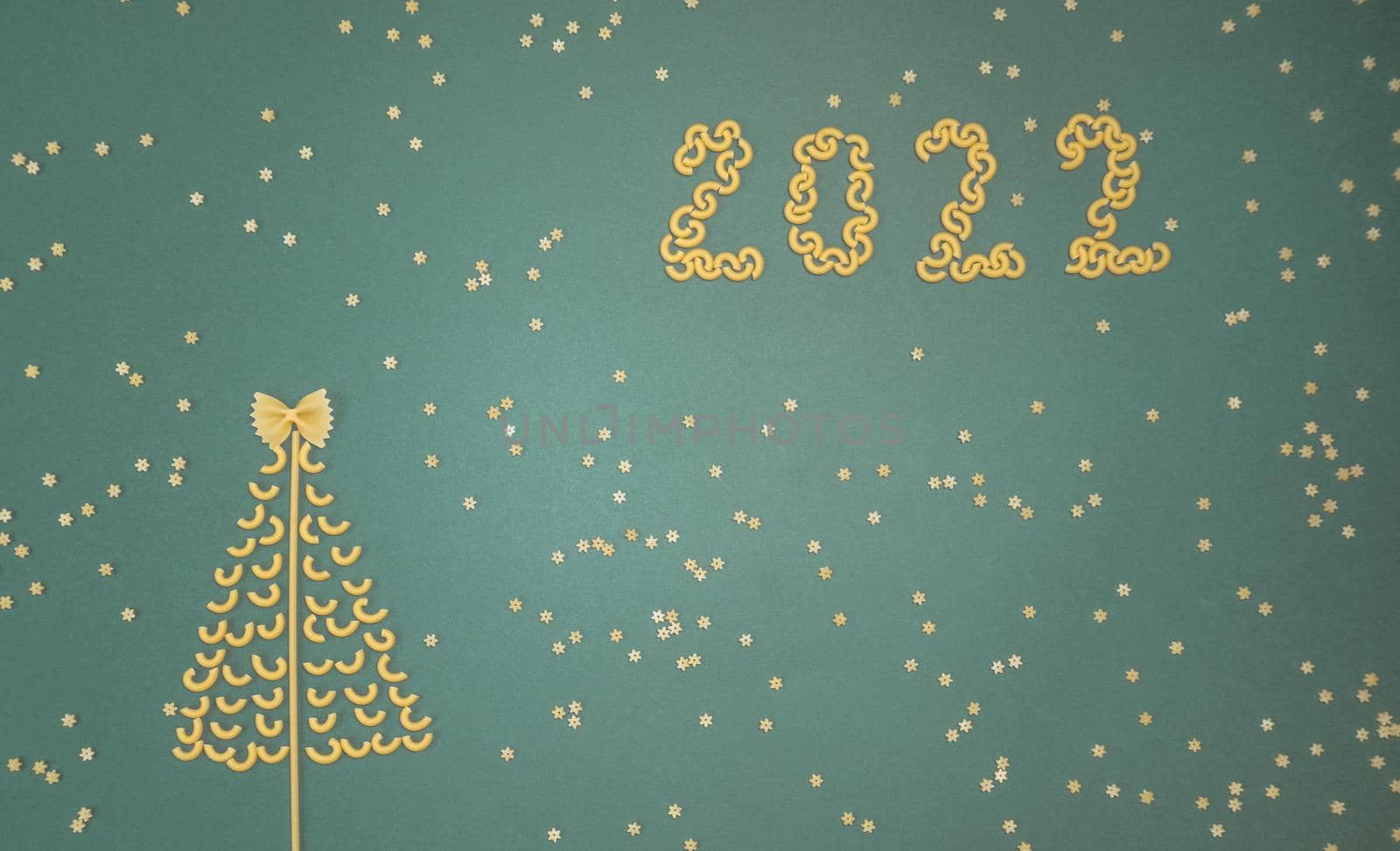 Christmas tree lined with dry pasta and numbers 2022 and stars from pasta on a green paper background. by Ekaterina34