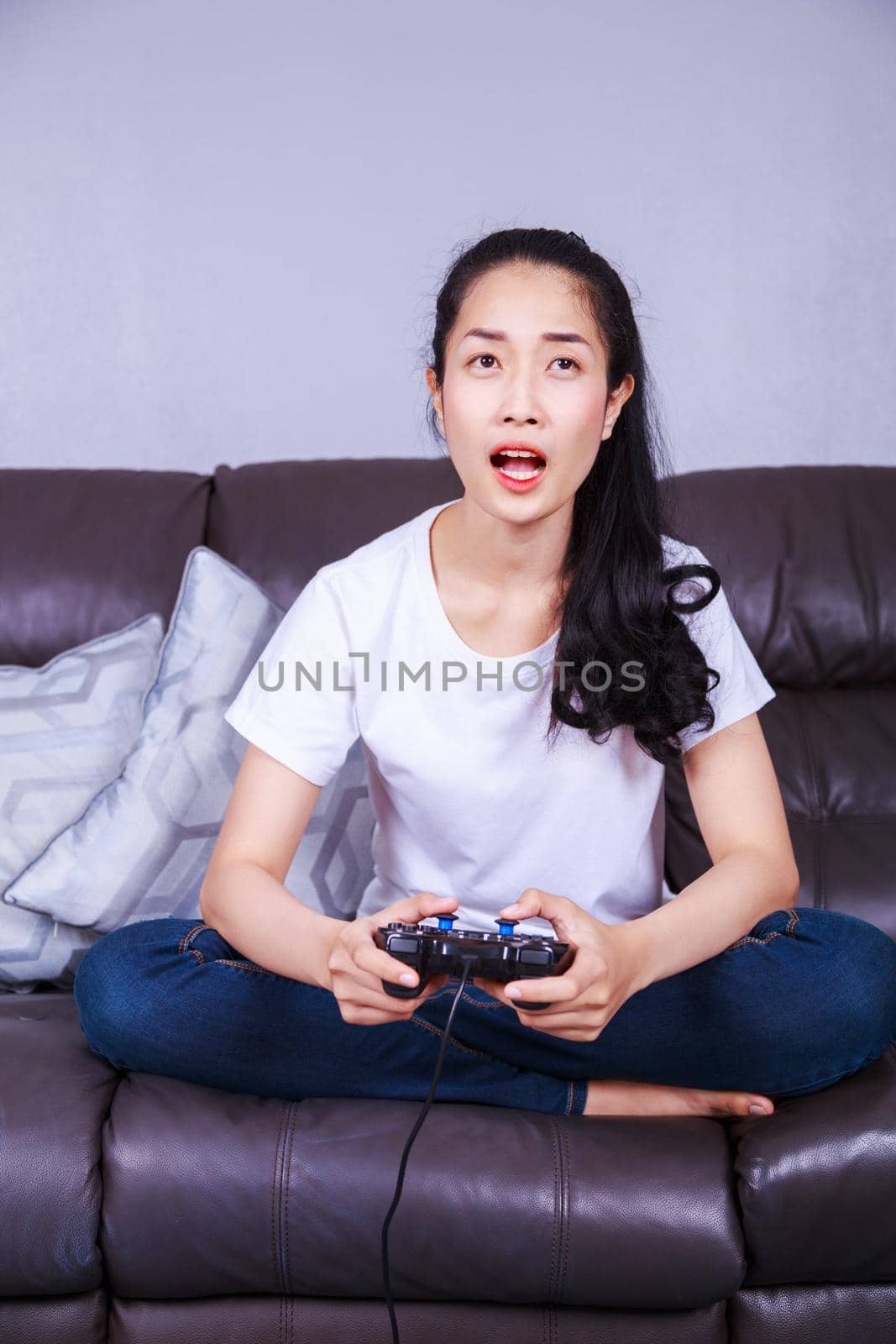 woman using joystick controller playing video game on sofa in living room at home