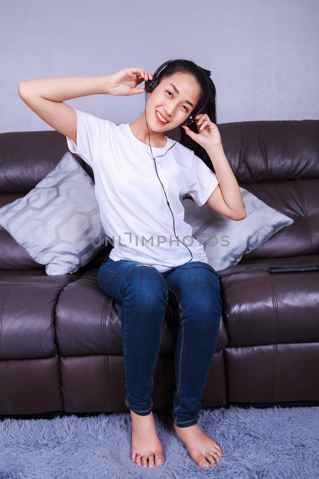 young woman listening to music in headphones with moblie on sofa at home