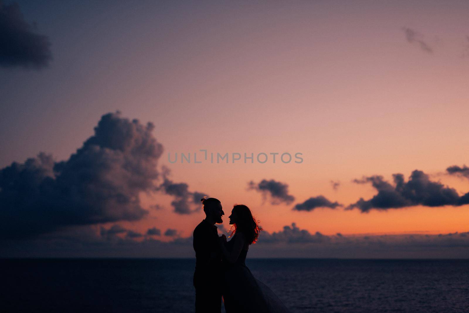 silhouettes of a happy young couple guy and girl on a background of orange sunset in the ocean