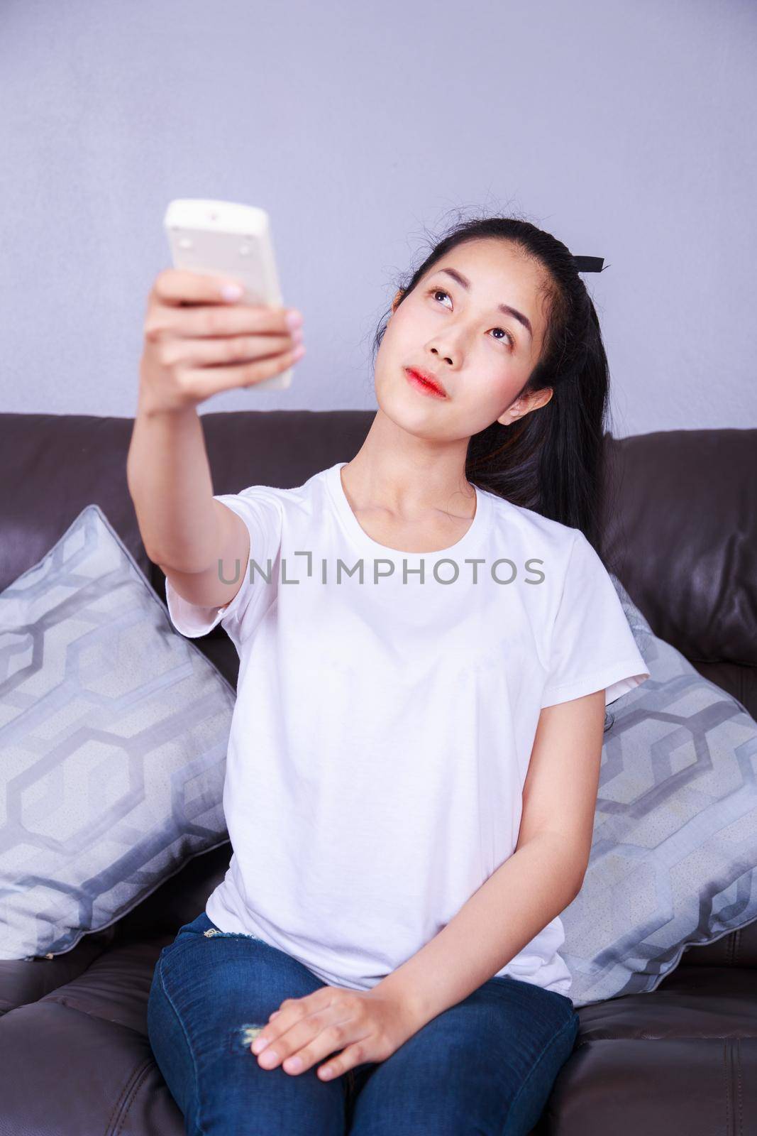 young woman holding a remote control air conditioner on sofa at home