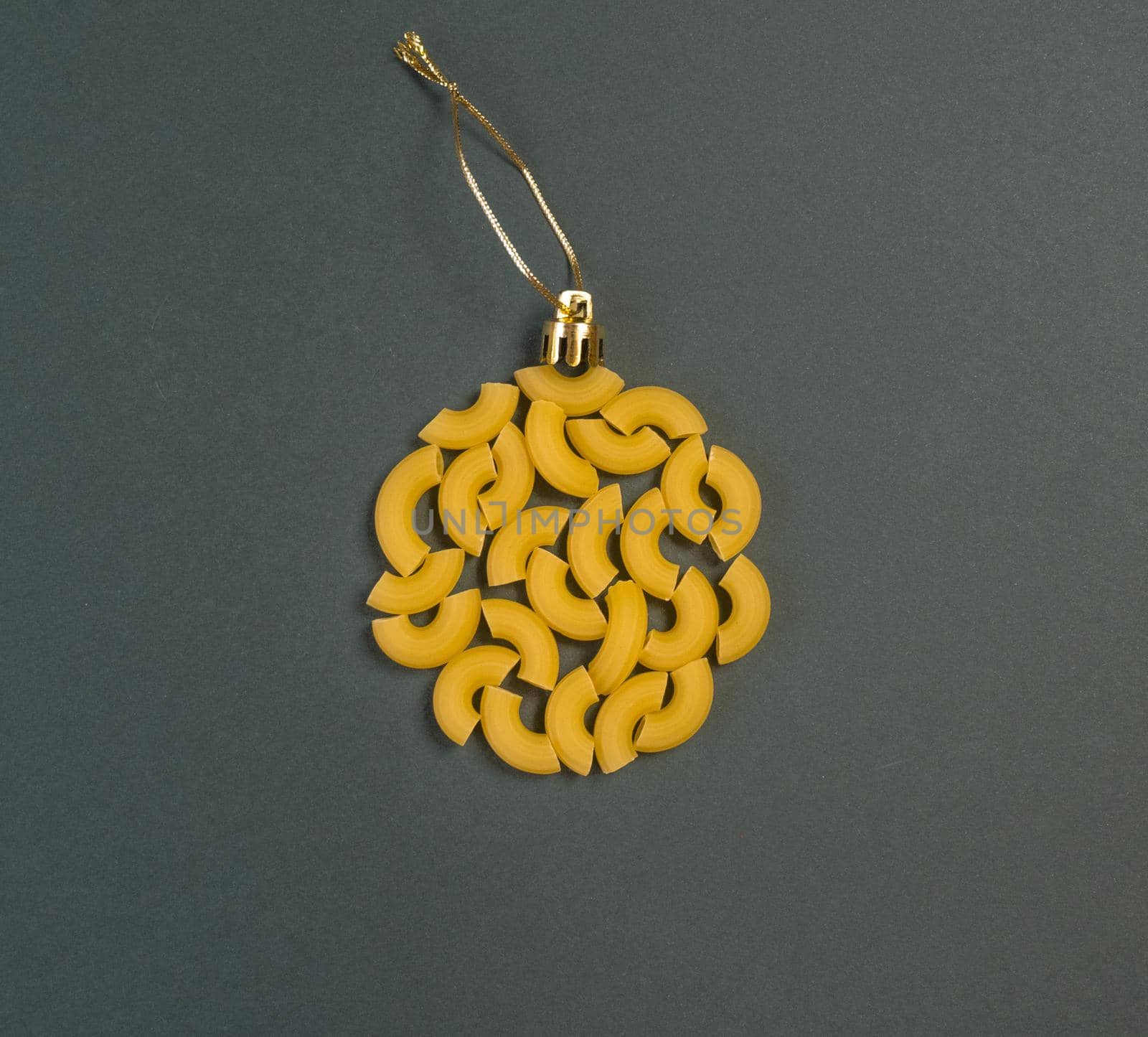 Christmas decoration on a tree in the form of a ball of pasta on a dark gray paper background, top view. Conceptual photo