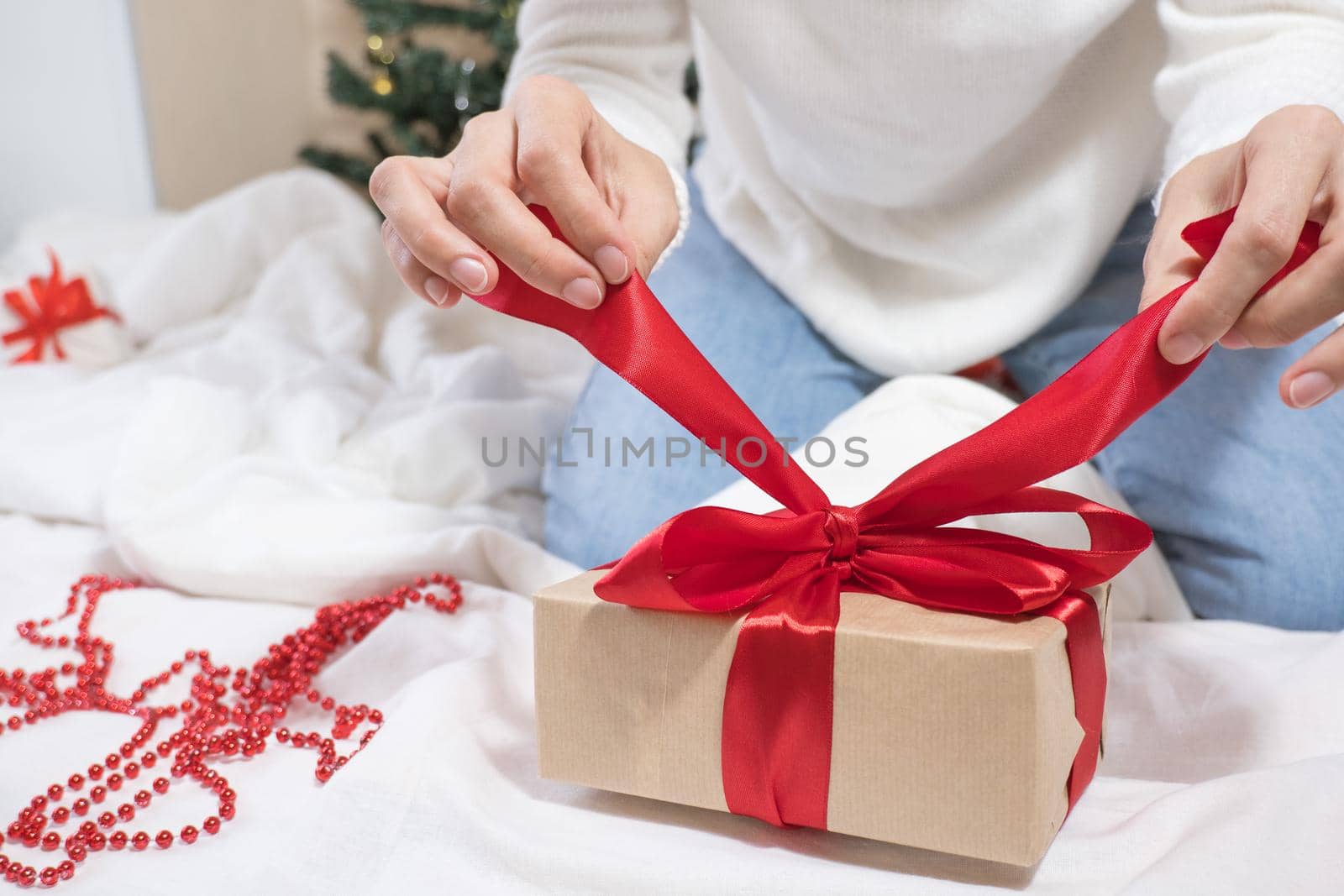 Happy Holidays. Female hands untie a bow on a gift box for Christmas in a white bed