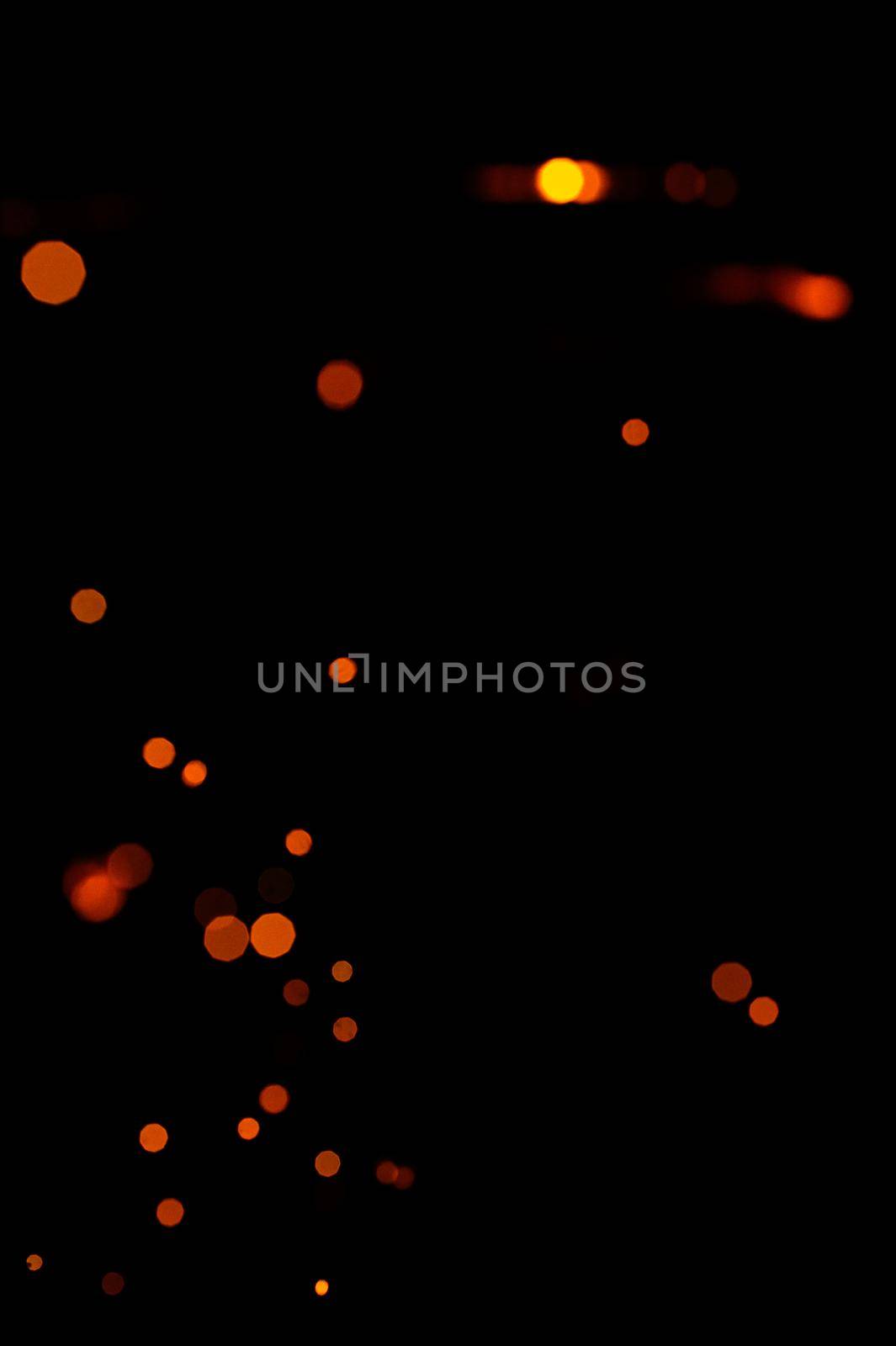 Orange bokeh on a black background, burning and blurred sparks from the fire. Particles of burning embers fly and glow isolated in the night sky 2021.