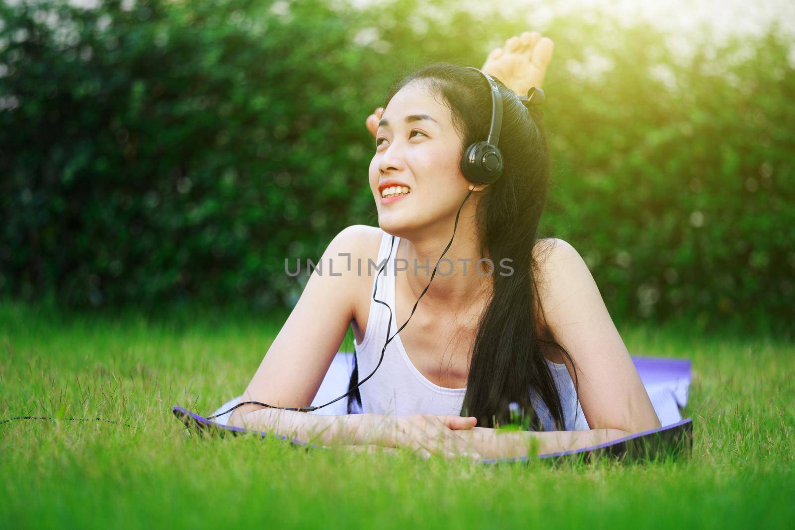 young woman listening to music with headphones and laying on a grass field