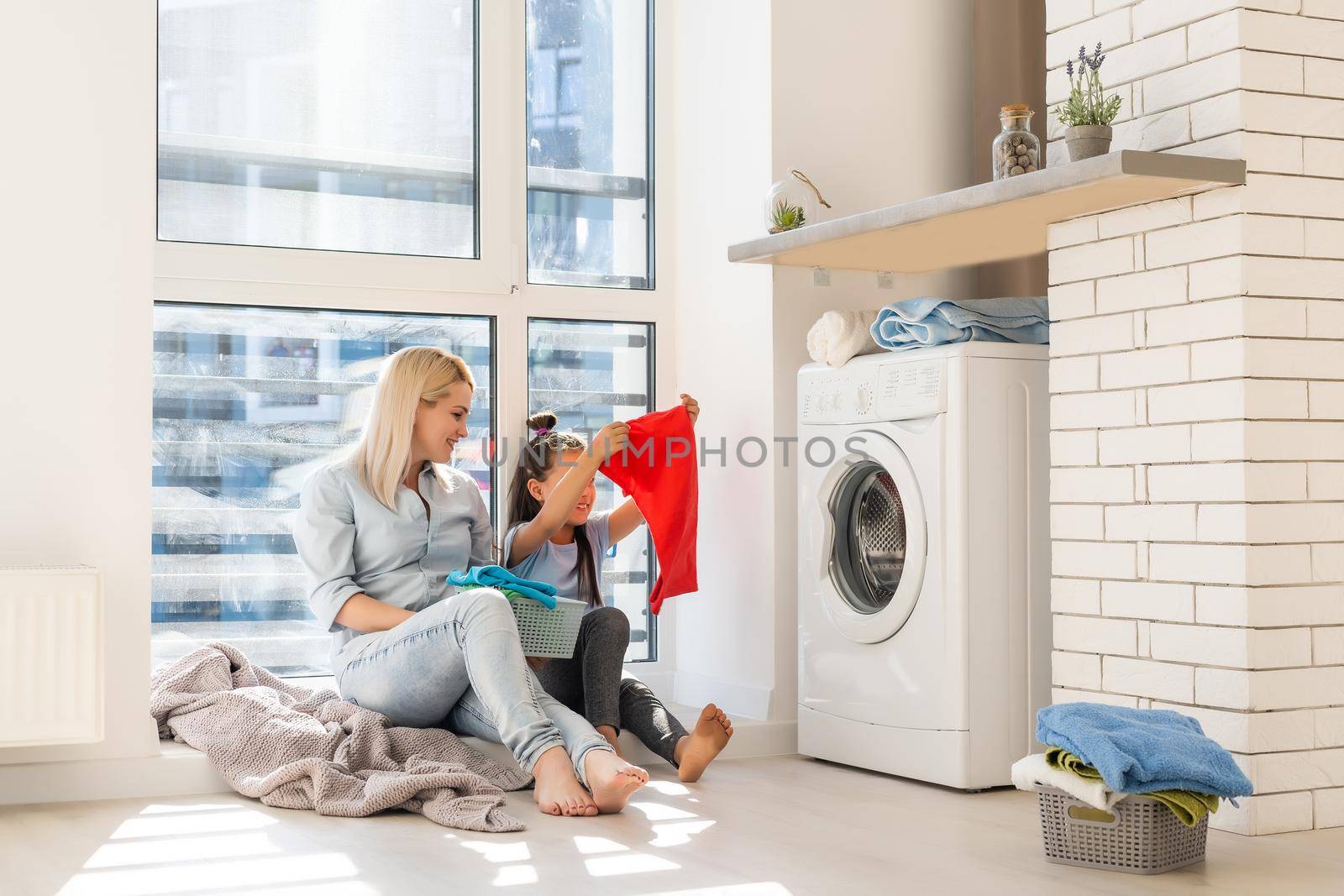 Happy housewife and her daughter with linen near washing machine