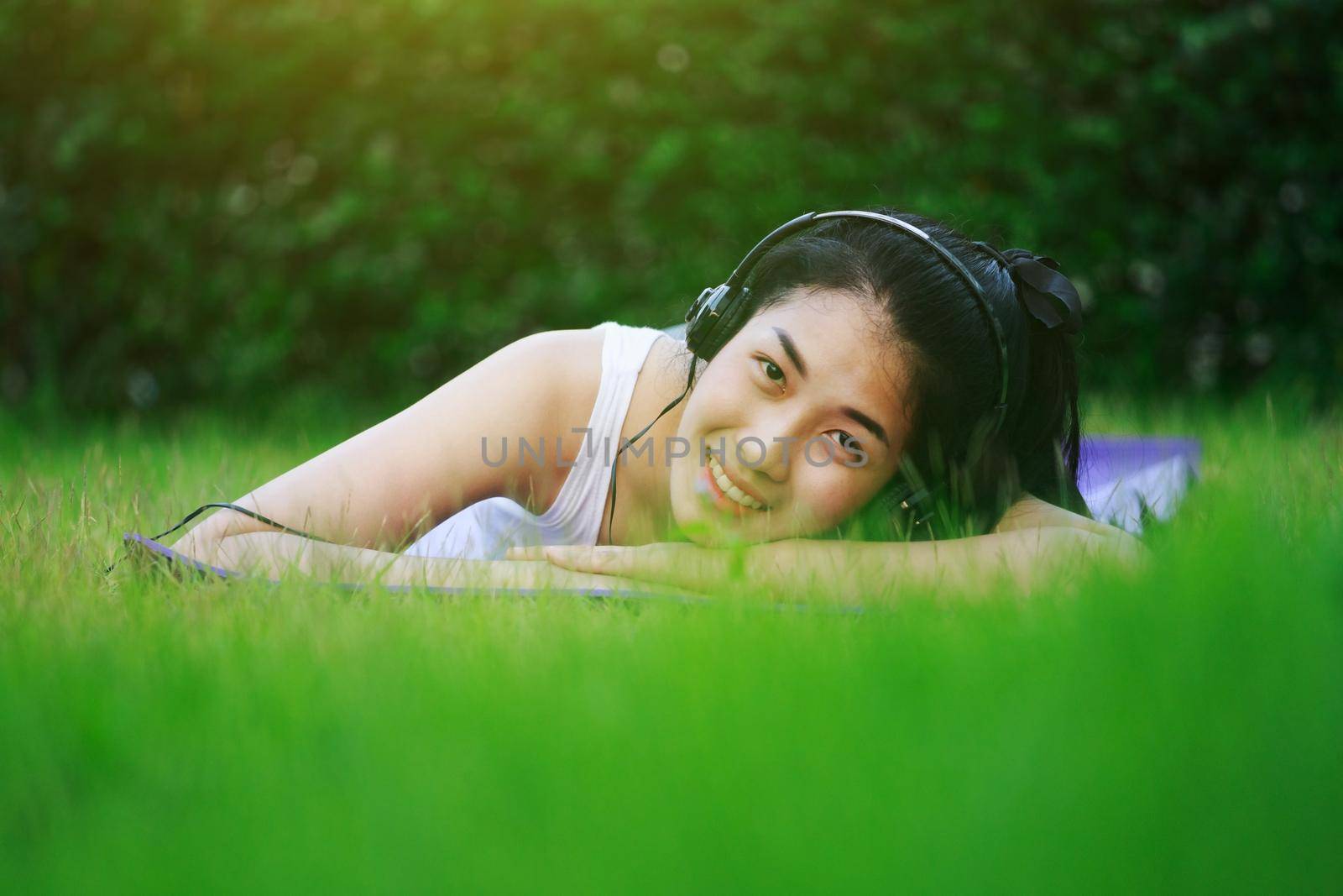 young woman listening to music with headphones and laying on a grass field