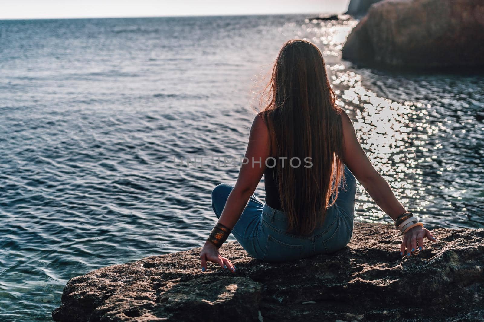 Young woman in swimsuit with long hair practicing stretching outdoors on yoga mat by the sea on a sunny day. Women's yoga fitness pilates routine. Healthy lifestyle, harmony and meditation concept.