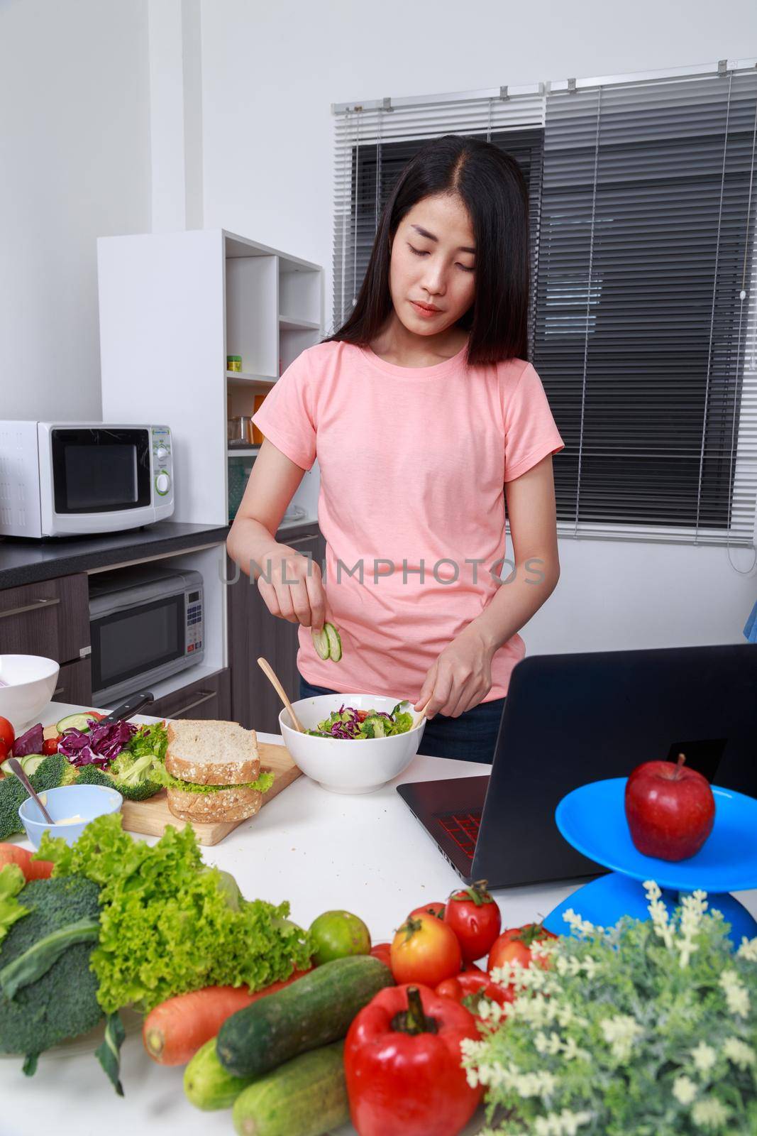 young woman mixing salad while cooking with laptop in kitchen 