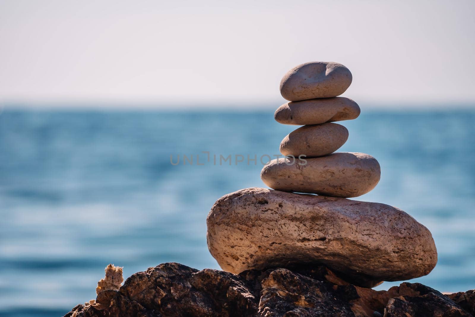 Pyramid stones on the seashore on a sunny day on the blue sea background. Happy holidays. Pebble beach, calm sea, travel destination. Concept of happy vacation on the sea, meditation, spa, calmness. by panophotograph
