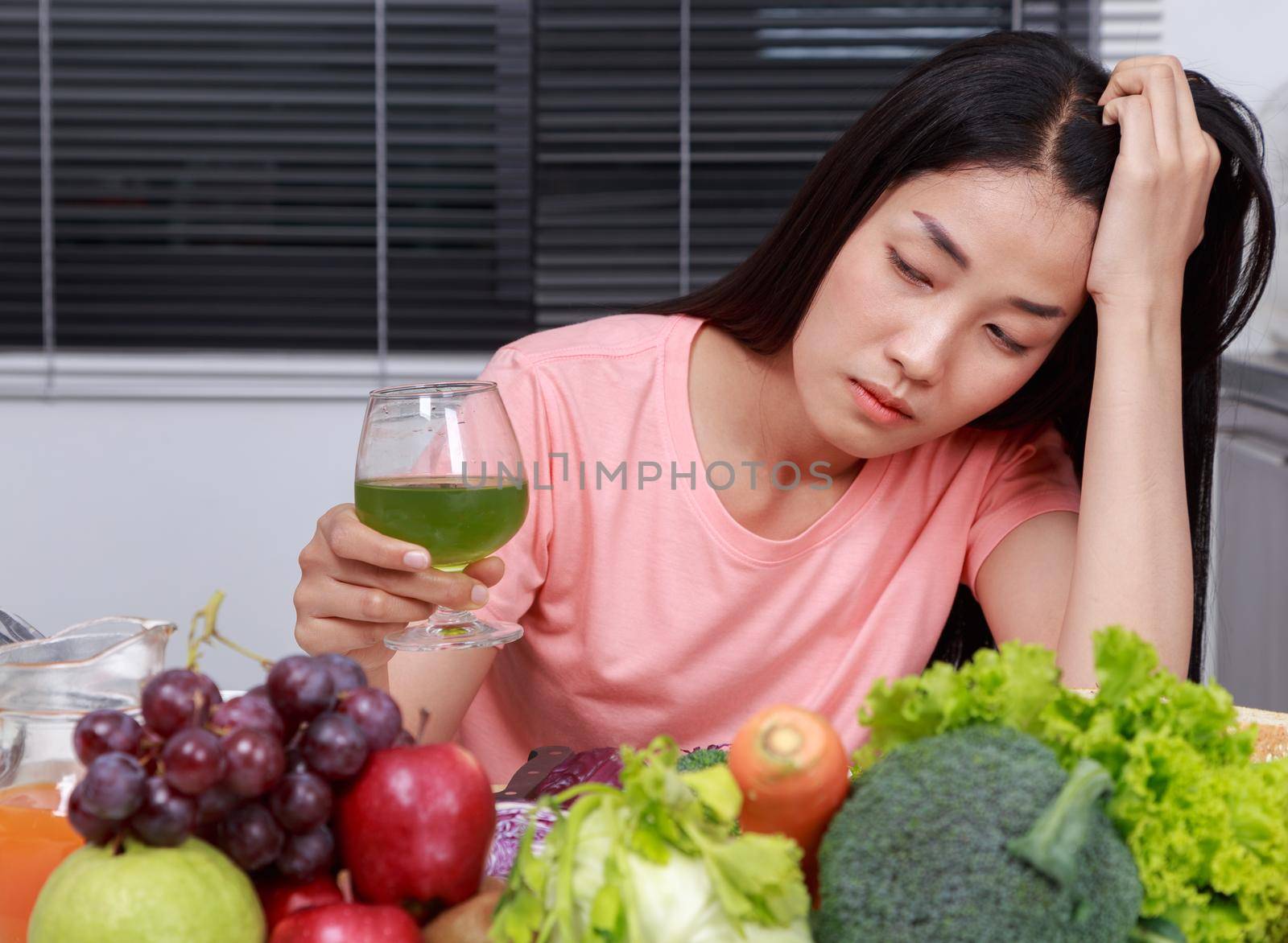 unhappy young woman drinking vegetable juice in kitchen