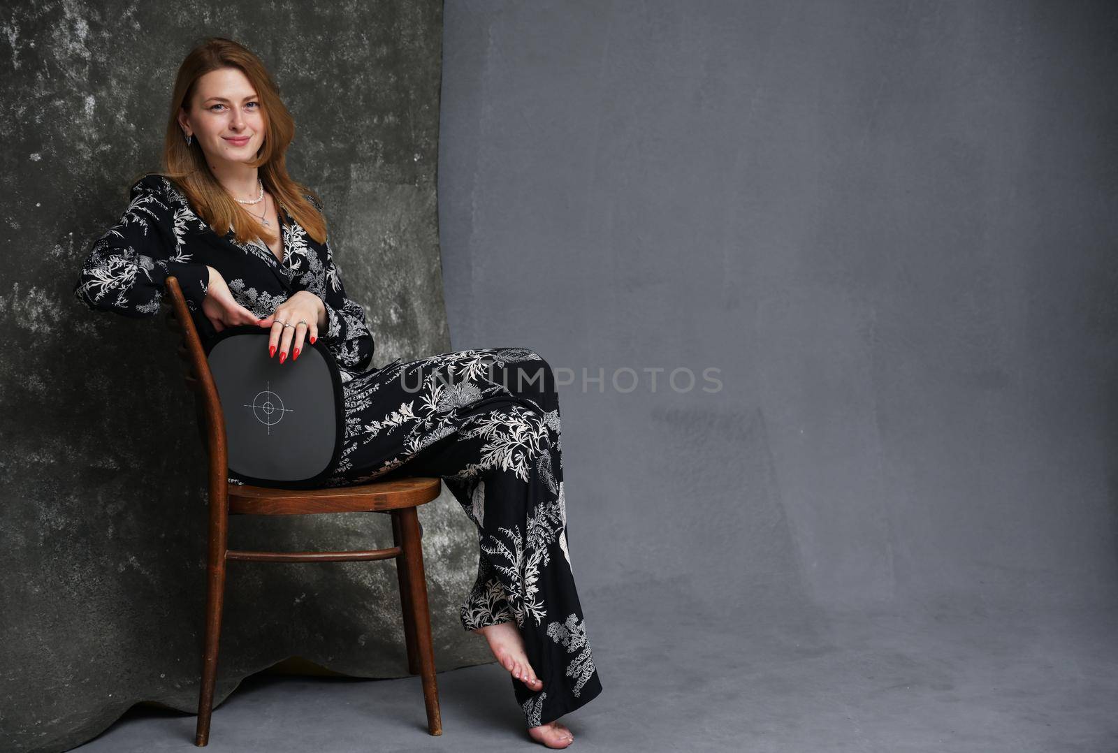 slim woman in dark clothes with a smile sits on a chair in the studio on a gray background